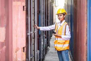 ung självsäker kvinnlig ingenjör som använder radiokommunikation och bär gul skyddshjälm och kontrollerar kontrolllastningsbehållare från lastfartyg för import och export foto