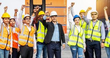 lastcontainerarbetare eller grupp av anställda express räckte upp sina händer för att uttrycka sin glädje för att fira framgången med sitt arbete. med en kran och en containerhög i bakgrunden foto