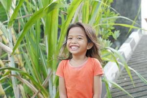 glad uttryck indonesisk liten flicka med löst hår på sockerrör bakgrund foto
