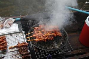 kyckling som klämmer bambu på galler grillar och röker, thaimat, säljer i träbåt i kanalen, thailand. foto