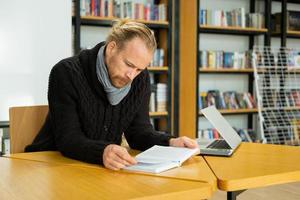 stilig man läser bok och arbetar i modernt bibliotek foto