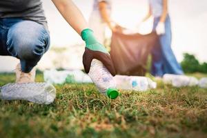 kvinna hand plocka upp sopor plastflaska för rengöring i parken foto