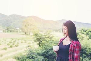 porträtt av den vackra kvinnan som håller en kopp kaffe på morgonen, bergsvy bakom. foto