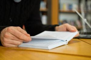 stilig man läser bok och arbetar i modernt bibliotek foto