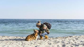 ung glad kvinnlig promenad med söt corgi hund på höstens soliga strand foto