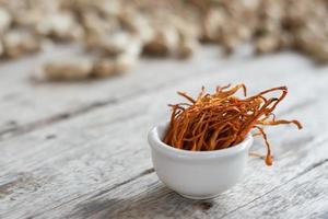 torr cordyceps militaris mycelium i vit skål med trä bakgrund. apelsin medicinsk svamp för god hälsa. foto