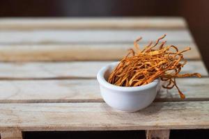 torr cordyceps militaris mycelium i vit skål med trä bakgrund. apelsin medicinsk svamp för god hälsa. foto