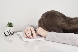 trött ung kvinna sover vid bordet med böcker, trötthet efter skolan eller jobbet foto