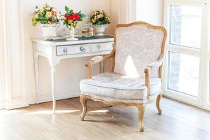 vackert lyxigt klassiskt vitt ljust rent inre sovrum i barockstil med stort fönster, fåtölj och blomkomposition. foto