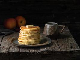 pannkaka med smör och en kopp te. mörk lynnig gammal rustik träbakgrund. foto