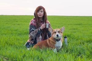 ung kvinna i poncho med corgi hund avkopplande i våren fält foto