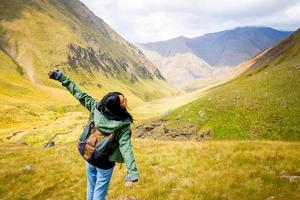 baksidan av kvinnlig kvinna med utbredd hand av glädje tittar på vackra bergslandskap foto