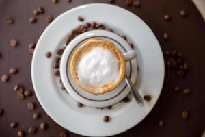 cappuccino med fint skummande skum. latte art med ett hjärta tillverkat av mjölk. kaffekopp med ett fat och en tesked på ett bord. foto