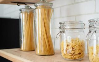 vete italiensk pasta i glasburk på en trähylla i köket. foto