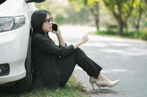 en ung asiatisk kvinna ringer sin servicetekniker för att laga en trasig bil vid sidan av vägen foto
