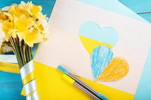 hjärta klippt ur papper och målat i blå och gula färger och gula vårblommor på träbaksida. kreativitet foto