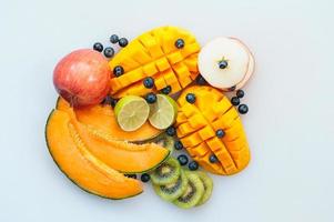 sortiment av saftig tropisk frukt på vit bakgrund. skivor på melon, apelsinmango, kiwi, lime, blåbär och äpple. vegetarisk maträtt. foto