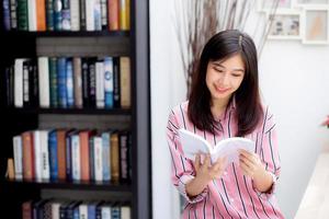 vacker av porträtt ung asiatisk kvinna koppla av sittande läsa bok i vardagsrummet hemma, flicka studera litteratur, utbildning och llifestyle koncept. foto