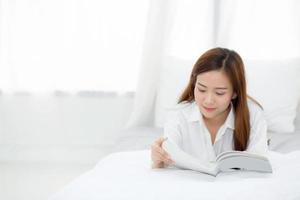 vacker av porträtt ung asiatisk kvinna koppla av liggande läsbok på sovrummet hemma, flicka studera litteratur, utbildning och livsstilskoncept. foto
