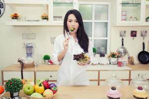 vacker ung kvinna som äter en hälsosam sallad i köket foto