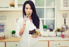 vacker ung kvinna som äter en hälsosam sallad i köket foto