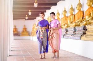 attraktiva thailändska kvinnor i traditionell thailändsk klänning håller färska blomstergirlanger för att komma in i ett tempel baserat på songkran festivaltraditionen i thailand foto