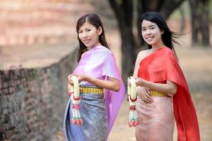 attraktiva thailändska kvinnor i traditionell thailändsk klänning håller färska blomstergirlanger för att komma in i ett tempel baserat på songkran festivaltraditionen i thailand foto