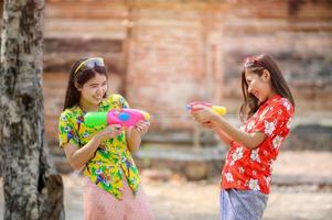 vackra asiatiska kvinnor håller plastvattenpistoler vid ett gammalt tempel under songkran, den vackraste och roligaste vattenfestivalen i thailand foto