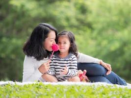 asiatisk liten flicka sitter med sin mamma på tyget, koppla av och lär sig utanför skolan för att njuta i naturparken foto