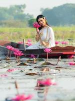 en elegant thailändsk kvinna som bär traditionella thailändska kläder bär lotusblommor som samlats in från ett lotusfält foto