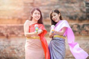 vackra asiatiska kvinnor håller plastvattenpistoler vid ett gammalt tempel under songkran, den vackraste och roligaste vattenfestivalen i thailand foto