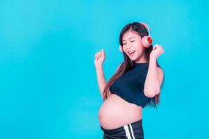 asiatisk vacker gravid kvinna står avslappnad och tycker om att lyssna på musik i hörlurar anslutna till internet foto