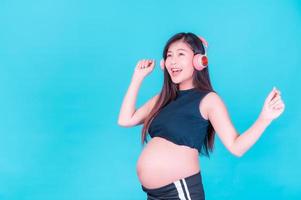 asiatisk vacker gravid kvinna står avslappnad och tycker om att lyssna på musik i hörlurar anslutna till internet foto