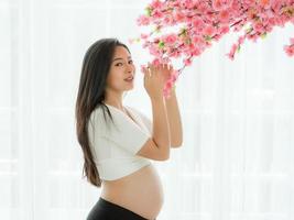 gravid vacker kvinna står för att hålla blommor i ett rum i japansk stil foto