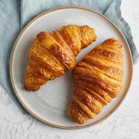 två läckra croissanter på tallrik och varm dryck i mugg. morgon fransk frukost foto