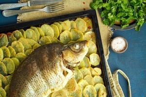 bakad karp, hel fisk från ugnen med skivad potatis på en stor bricka. traditionell polsk maträtt foto