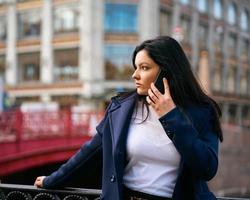 kvinna med långt hår pratar i telefon. höst eller vinter, flicka i utomhus. vacker intelligent brunett på gatan i Saint-Petersburg i centrum nära bron, kopieringsutrymme foto