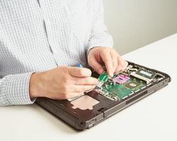 man reparerar dator. en serviceingenjör i skjorta reparerar laptop, vid vitt skrivbord mot vit vägg. foto