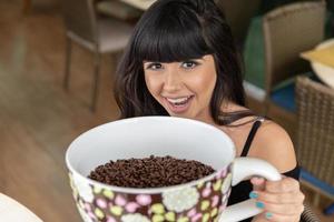 vacker brunett tjej med en stor keramisk mugg med kaffefrön. hög av kaffebönor i kopp. foto