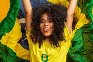 afro flicka hejar på favorit brasilianska laget, håller flaggan i gul bakgrund. foto