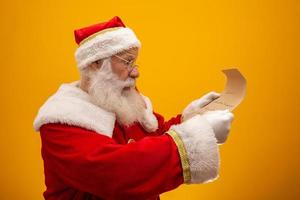 glad jultomte håller vintage papper på gul bakgrund. god jul och nyårsafton koncept. kopieringsutrymme. svårigheter att läsa. ful handstil. foto