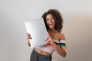 porträtt av leende ung afroamerikansk kvinna som håller bärbar dator över vit bakgrund foto