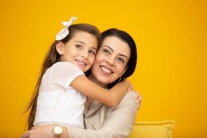 glad mors dag närbild porträtt av vackra, charmiga mor och dotter med strålande leenden över gul bakgrund. dotter kramar mamma på gul bakgrund. foto