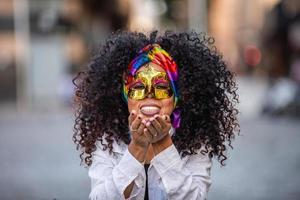 karnevalsfest. brasiliansk lockigt hår kvinna i kostym blåser konfetti foto