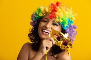 vacker kvinna klädd för karnevalskväll. leende kvinna redo att njuta av karnevalen med en färgglad peruk och mask foto