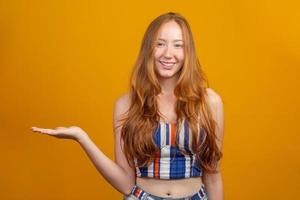 en rödhårig flicka på gul studiobakgrund erbjuder möjligheter att peka fingersidan på kopieringsfritt utrymme för reklaminnehållsannons. foto