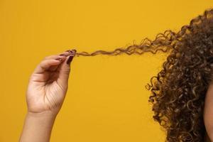 närbild amerikansk afrikansk kvinna som drar ett hårlock. lockigt hår på gul bakgrund. foto