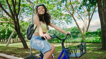 ung latinsk kvinna i skyddshjälm cyklar längs cykelvägen i en stadspark foto