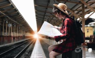 ung resenär kvinna tittar på kartor planerar resa på tågstationen. sommar och resor livsstilskoncept foto