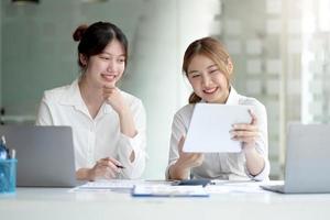 två unga asiatiska affärskvinnor diskuterar med nystartsprojektidépresentation, analyserar planering och finansiell statistik och investeringsmarknaden på kontoret. foto
